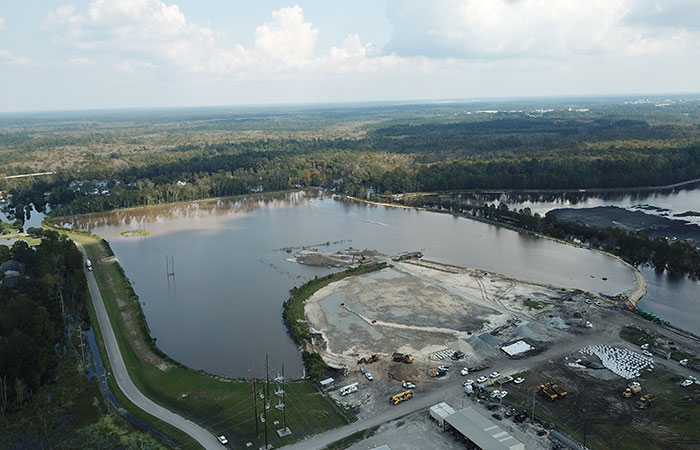 Aerial view of Grainger’s Ash Pond 1, which has been filled with water to equalize pressure on the dike from the rising waters of the Waccamaw River. In the foreground, mounds of stone and bags filled with stone are assembled.